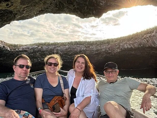 Vier Personen sitzen in einem Boot, das durch eine felsige Meereshöhle fährt